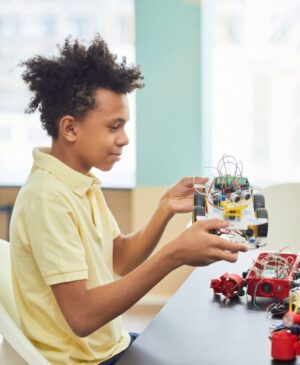 A young boy holds a robotic toy car indoors, focusing intently on learning and creativity.