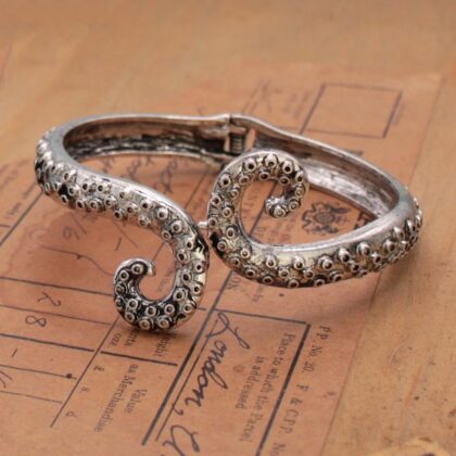 Antiqued silver-tone octopus tentacle cuff bracelet displayed on vintage paper, highlighting its curling shape and detailed suction cups.