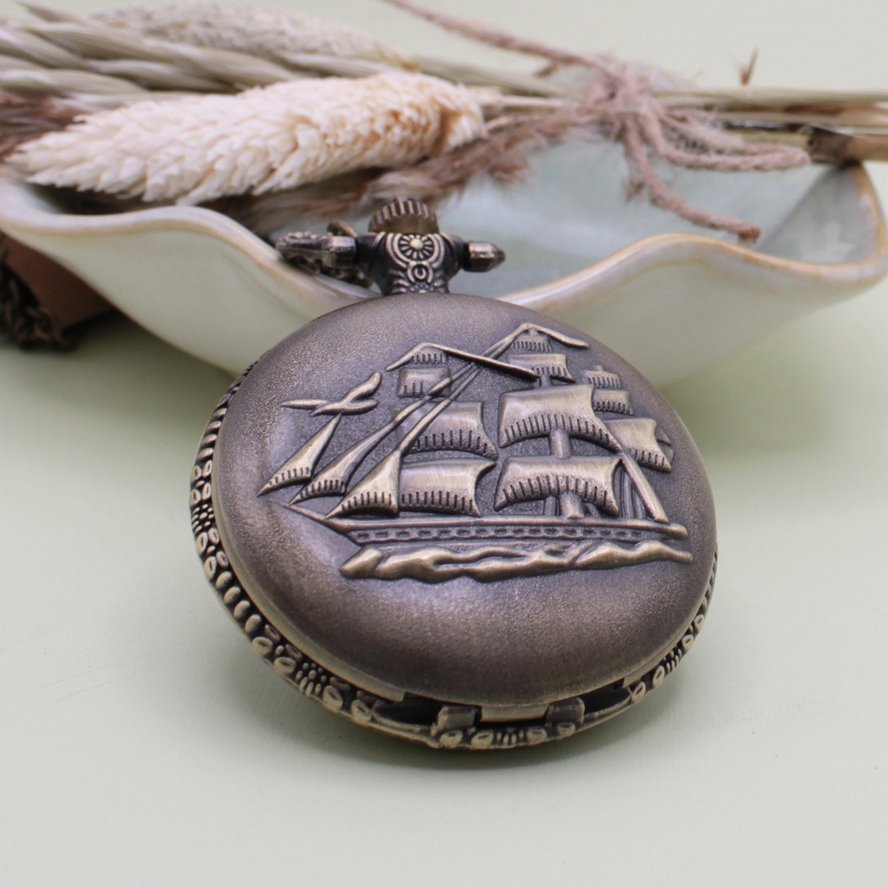 Close-up of the raised sailing ship design on the Ancient Mariner gold-tone pocket watch necklace.