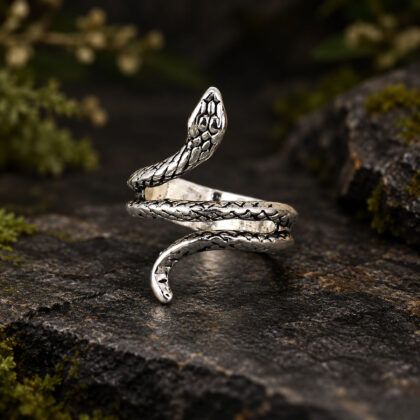 Antiqued silver-tone snake wrap ring displayed upright on a dark stone surface, showing the coiling serpent and detailed scale pattern.