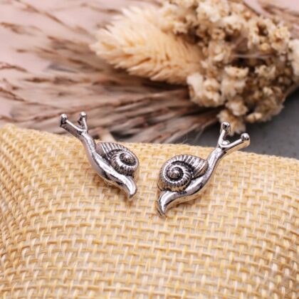 Pair of silver-tone snail stud earrings with detailed spiral shells displayed on a woven natural-texture surface.