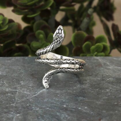 Antiqued silver snake wrap ring displayed on a dark stone surface with a coiled body and detailed scales.
