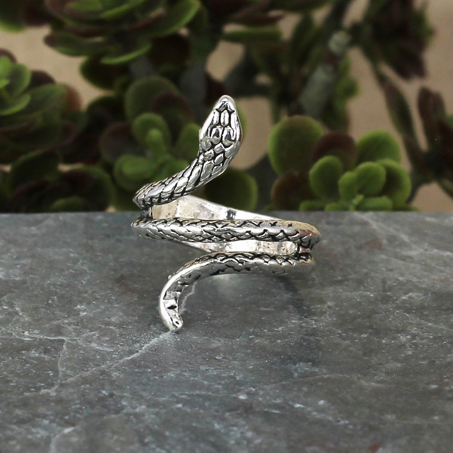 Antiqued silver snake wrap ring displayed on a dark stone surface with a coiled body and detailed scales.